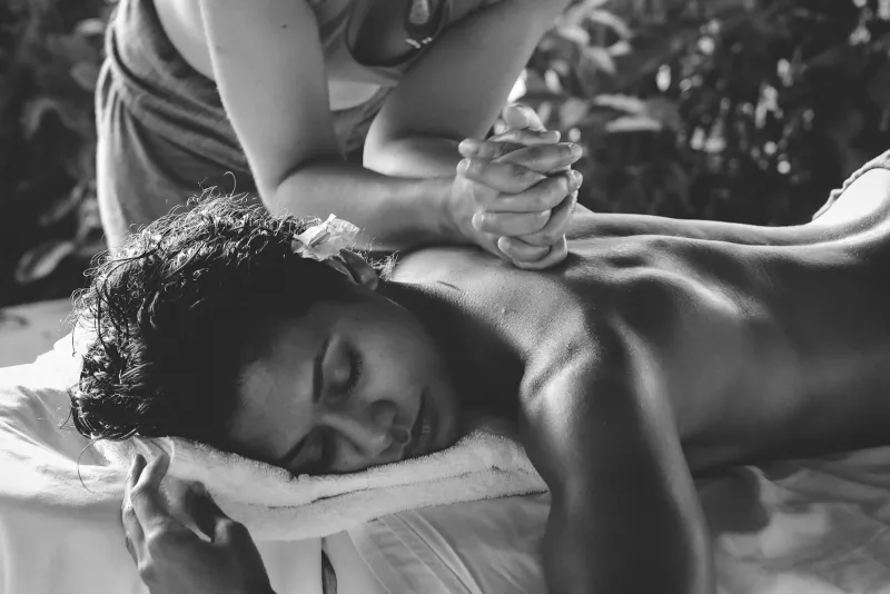 Masajista inclinada sobre la espalda de una persona recostada con los ojos cerrados, en blanco y negro